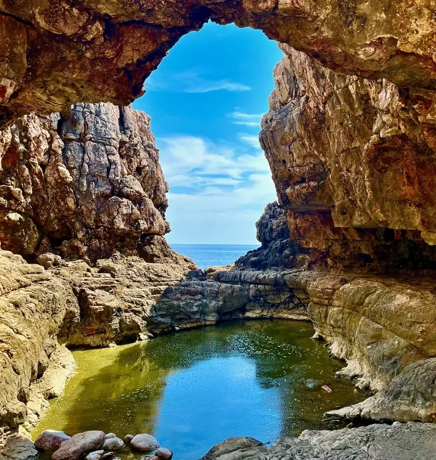 View from inside a cave on Lokrum Island, with sunlight illuminating the rugged rock walls and a serene, natural rock pool leading to the Adriatic Sea