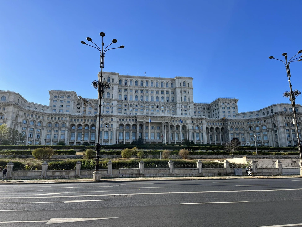 The imposing Palace of Parliament in Bucharest stands under a clear blue sky, showcasing its grand neoclassical facade with ornate detailing, a symbol of Romania's historical and political heritage.