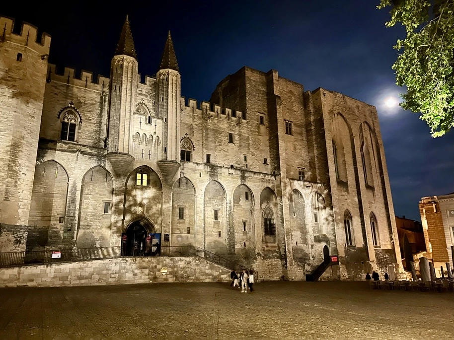 Palais des Papes in Avignon lit up at night time, illuminating the square.