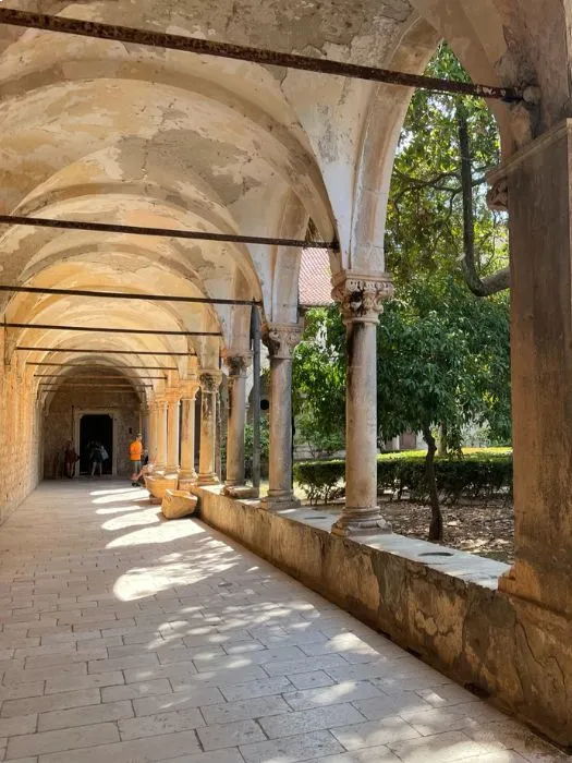 The cloister of the Benedictine Monastery on Lokrum Island, showcasing arched colonnades and a sunlit courtyard with trees