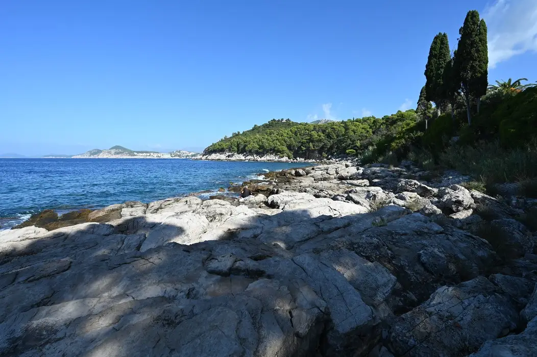 Rocky coastline of Lokrum Island with clear blue waters of the Adriatic Sea, framed by lush Mediterranean vegetation under a bright sky