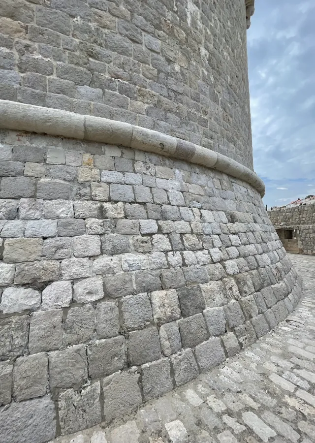 Close-up view of the textured limestone walls of Minčeta Tower in Dubrovnik, showcasing the medieval architecture with the overcast sky hinting at the atmospheric setting often seen in Game of Thrones.