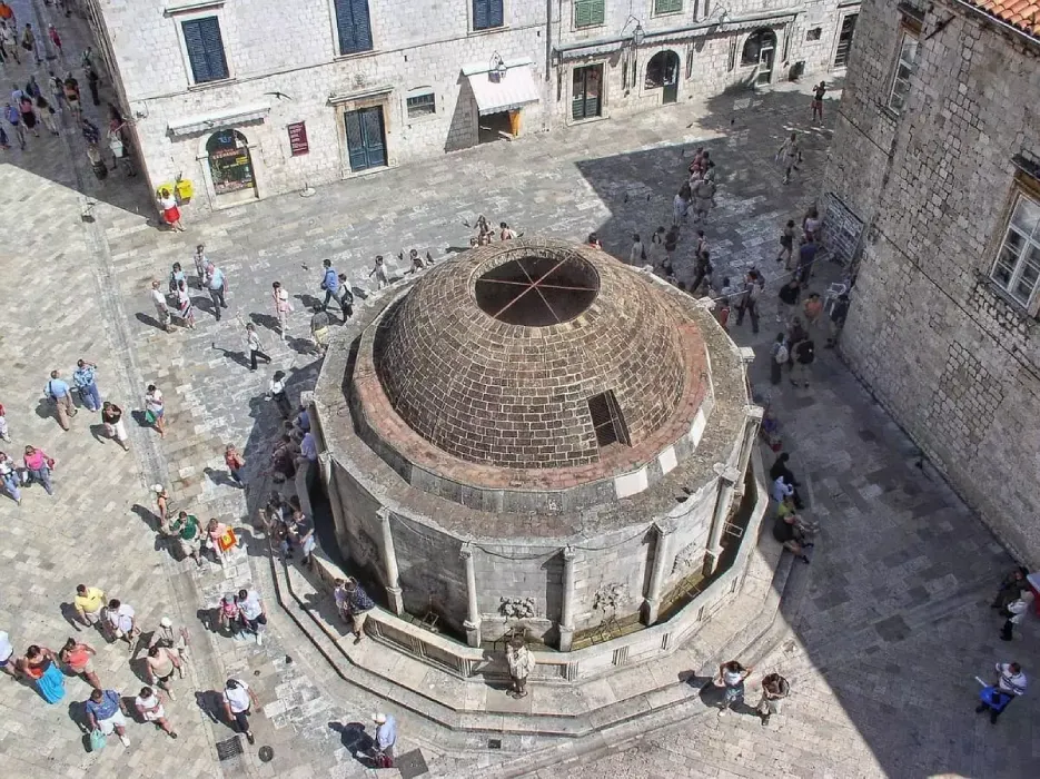 Aerial view of Onofrio's Large Fountain in Dubrovnik, Croatia, showing the distinctive circular architecture with visitors walking around and enjoying the old town square on a sunny day