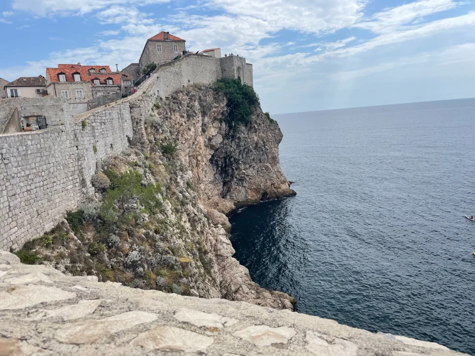 View of Dubrovnik's outer city walls towering over the Adriatic Sea, with red-tiled roofs of old town buildings against a serene sky