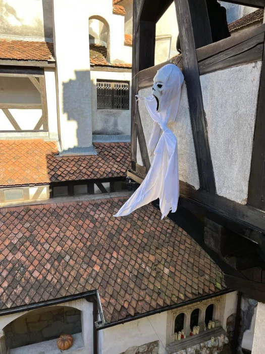 A ghost decoration with a white sheet and a screaming face hangs on the wooden beams of Bran Castle's courtyard, overlooking the classic terracotta roof tiles and stone walls.