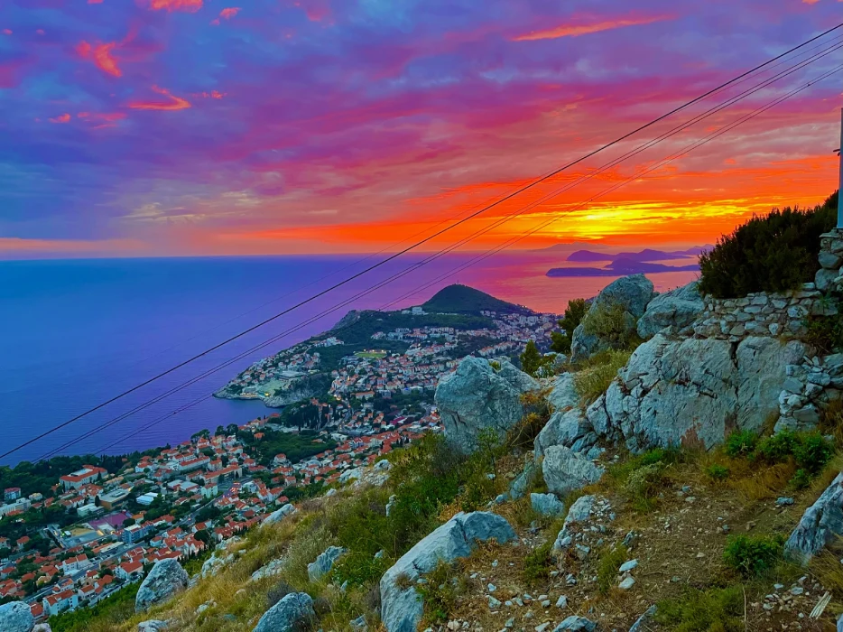 A breathtaking sunset view from Mount Srd, overlooking the coastal city of Dubrovnik with a scattered islands horizon, as vibrant pink and orange hues blend into the twilight sky above the Adriatic Sea