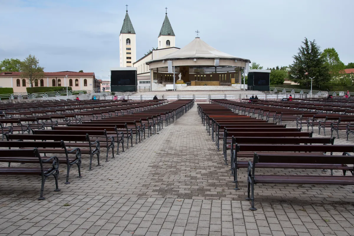 The Church of Saint James the Greater in Medjugorje, Bosnia and Herzegovina featuring rows of empty benches arranged for outdoor worship, leading up to the main church building.