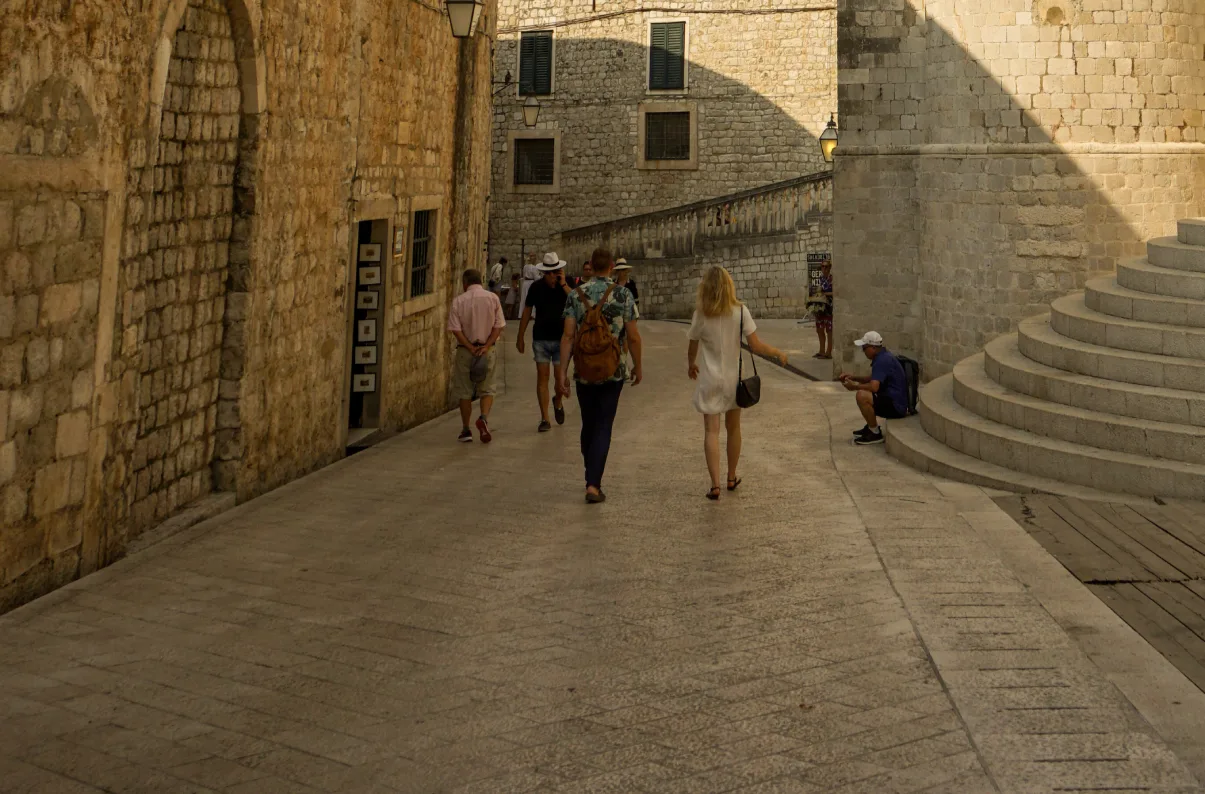 A crowd on St. Dominic Street in Dubrovnik with tourists walking along a cobblestone pathway, flanked by ancient stone buildings