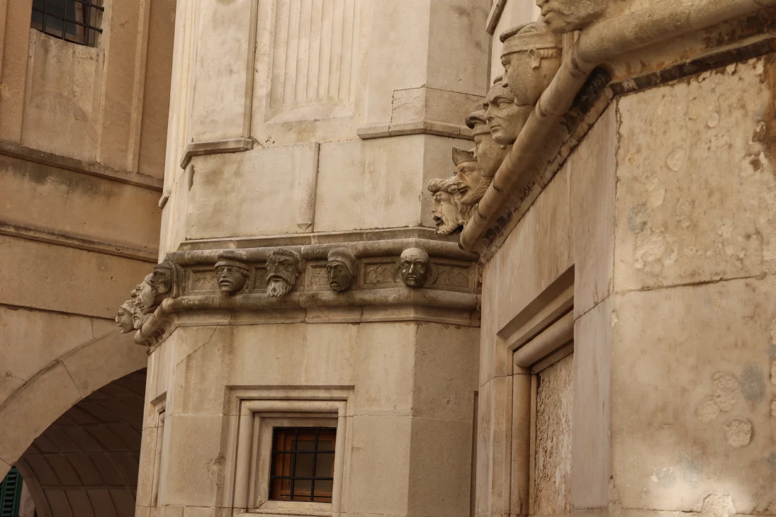 The exterior of the Cathedral of St. James in Šibenik. This features a detailed frieze with sculpted human faces. The stone carvings display a variety of expressions and headwear.