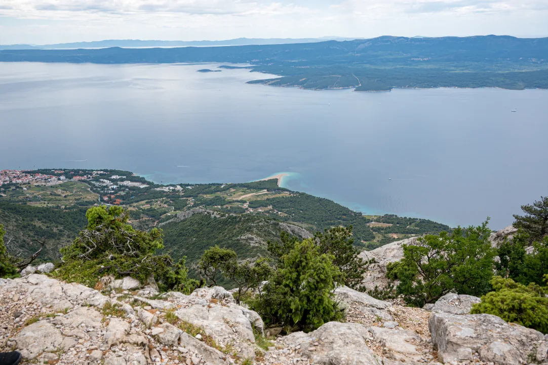 A stunning view from Vidova Gora Peak on Brač Island, overlooking a vast expanse of blue sea, green landscapes, and a distant coastline. The image captures the natural beauty and serene environment from the island's highest point.