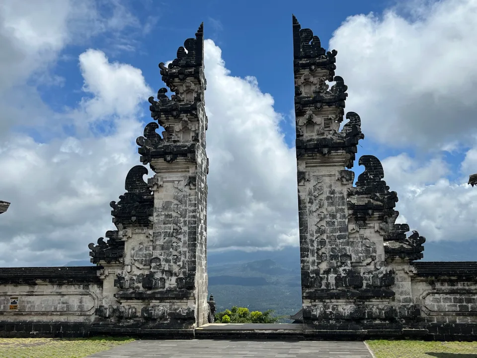 The Gates of Heaven in Bali, Indonesia. The intricate black-and-white stone gate stands against a backdrop of clouds and mount agung can be seen in the distance.