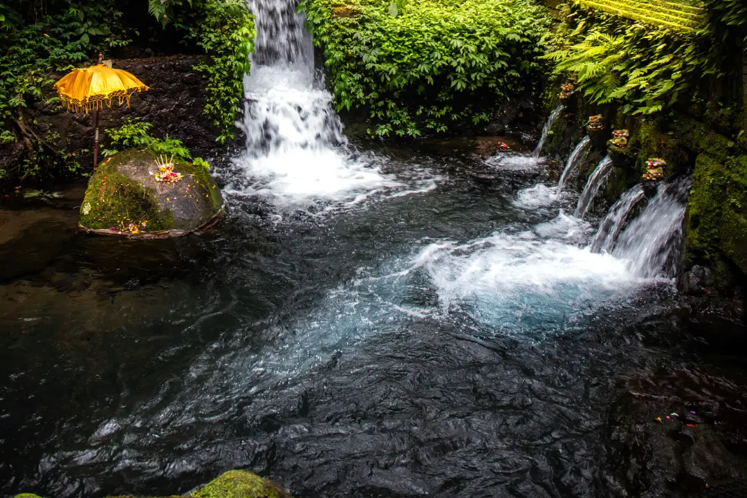 A natural spring at Mengening Temple in Bali, featuring cascading waterfalls and crystal-clear water surrounded by green foliage. 