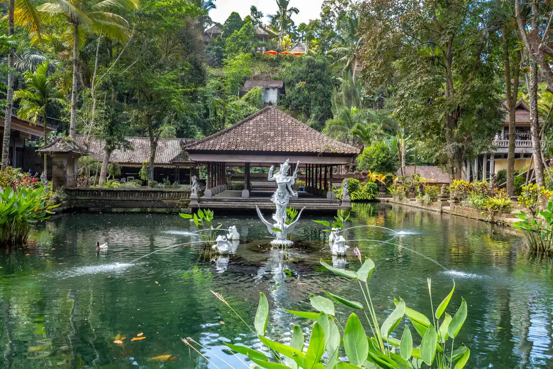 A pond surrounded by lush greenery at Pura Gunung Kawi Sebatu, Bali. The pond features a centrepiece statue of a deity with fountains and smaller statues of animals.