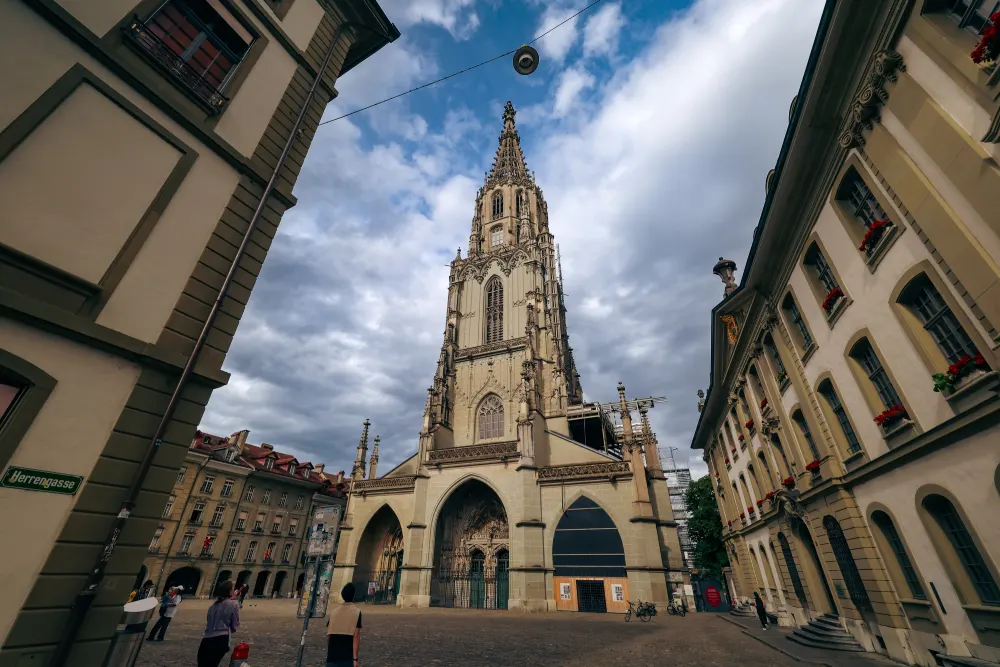 Wide-angle view of Bern Cathedral in Switzerland, with its tall Gothic spire reaching into a cloudy sky.