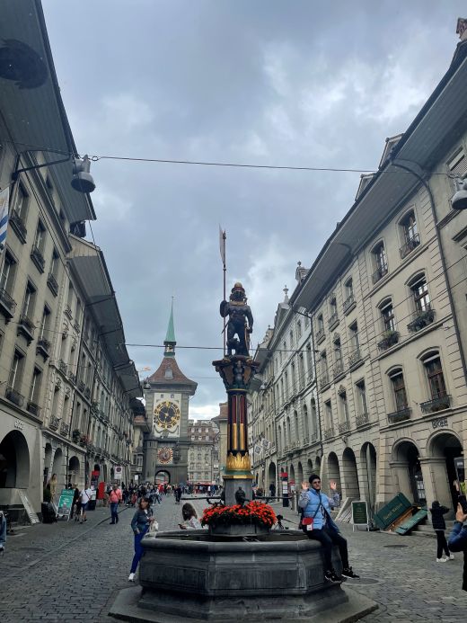 Statue of a bear in armor holding a banner and shield atop the Zähringerbrunnen Fountain in Bern’s Old Town, set along a cobblestone street.