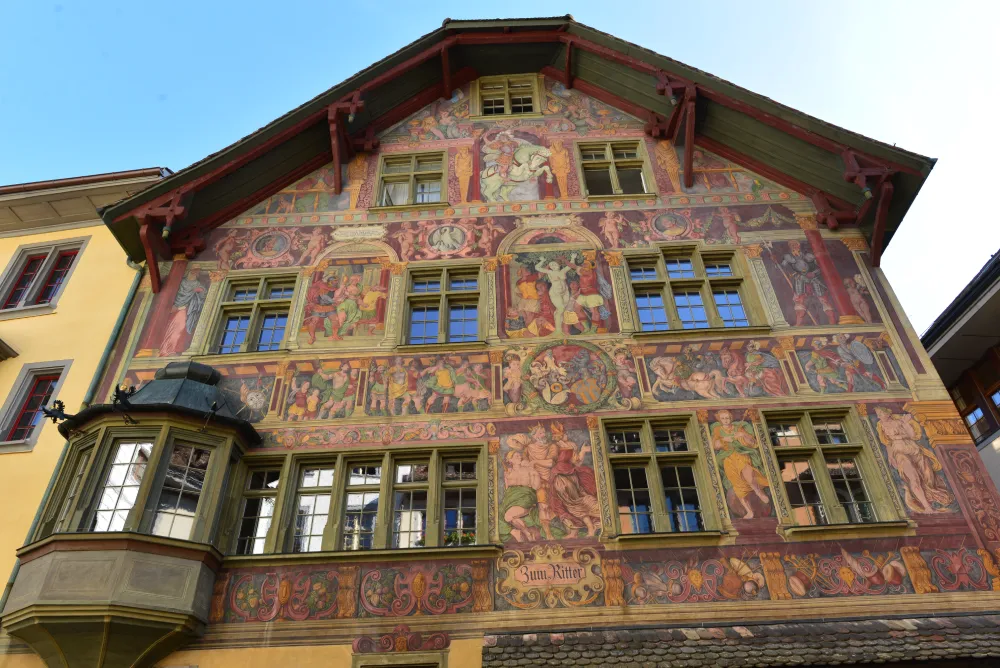 Colourful fresco-covered facade of the Haus zum Ritter in Schaffhausen, Switzerland, featuring detailed Renaissance-style paintings of historical and mythological scenes.