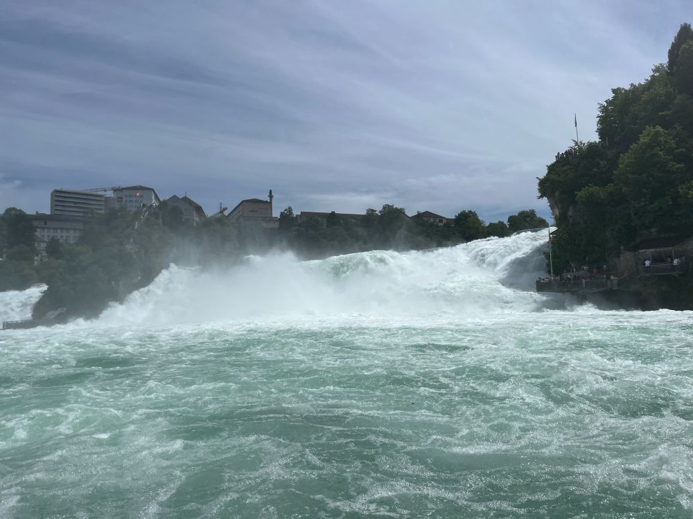 View of Rhine Falls from a boat, with splashing water in the foreground and mist rising from the powerful waterfall.