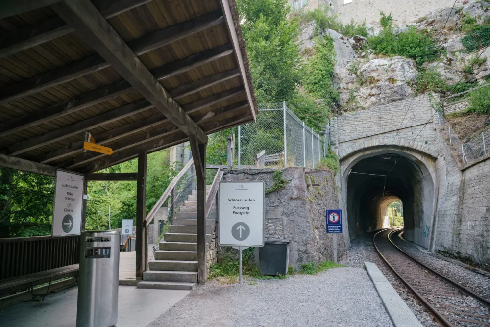 Covered walkway and signs at Schloss Laufen am Rheinfall near a railway tunnel and footpath entrance.