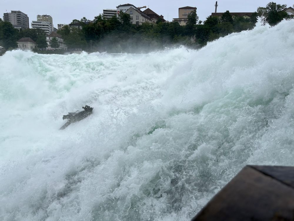 Looking out at Rhine Falls from the Känzeli platform, watching the waves crashing hard over the rocks with a viewing deck barely visible in the spray.