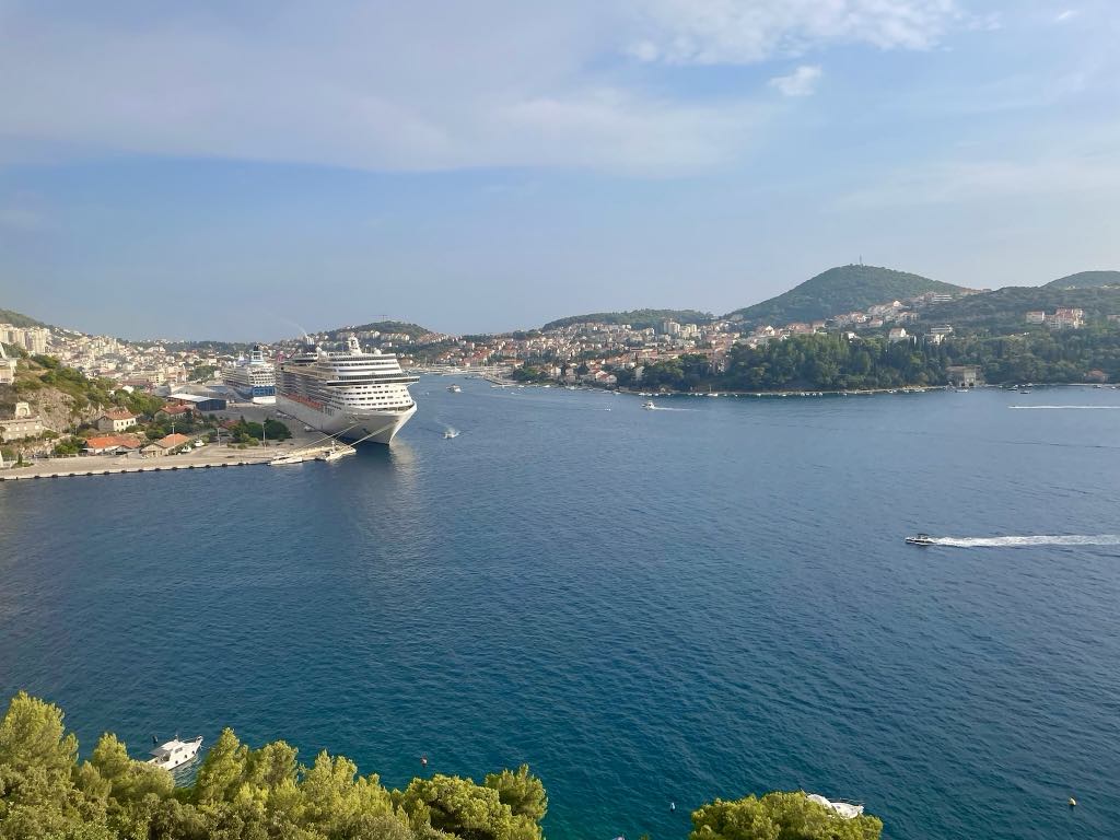 A large white cruise ship docked at the Port of Dubrovnik, Croatia, with another cruise ship behind it. 